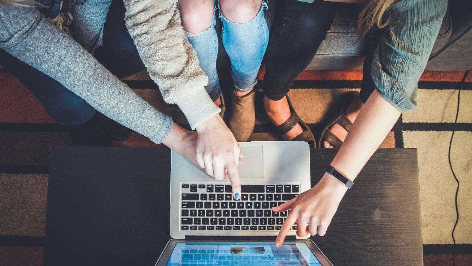 Three people sitting together and pointing at a laptop on a table.